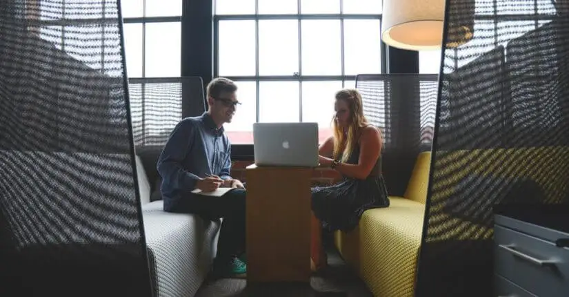 A man and woman sit on cushioned benches in a private space on either side of a narrow table. They share a computer and take notes.