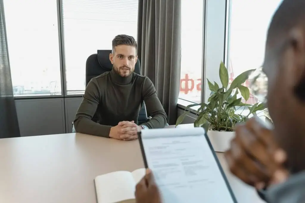 A man sitting in an interview across the table from an interviewer holding a clipboard—Stratice blog cover.