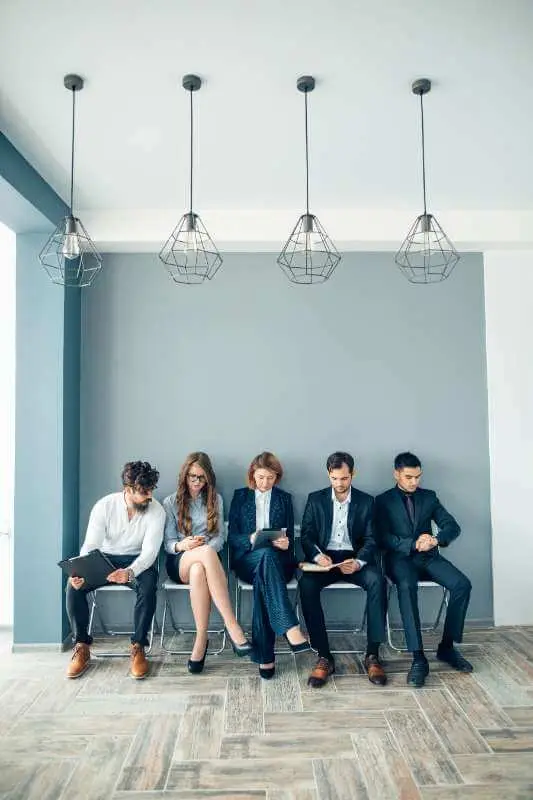 A row of potential hires sitting in chairs outside of an interview office. They are part of Stratice's Recruitment Process Outsourcing solutions.