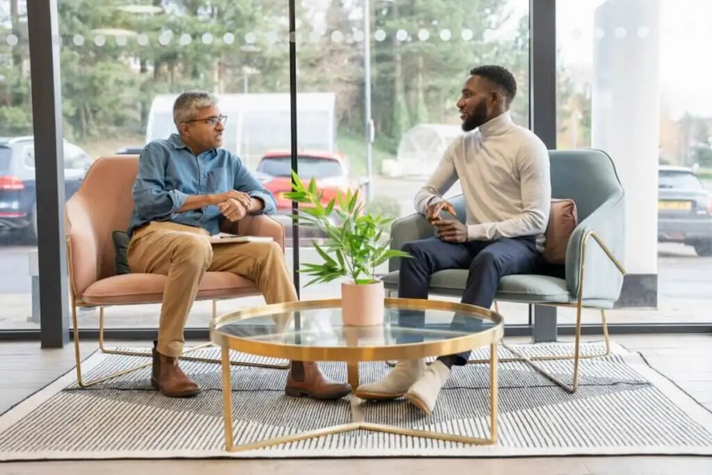 Two men sit in chairs in an office lobby and discuss Stratice's hiring services.